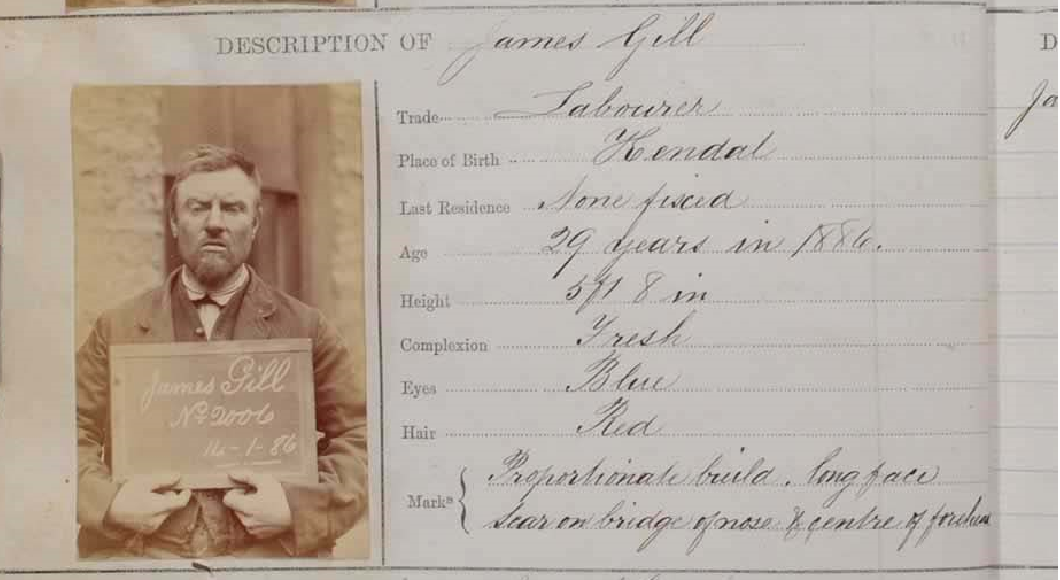 Form. A black and white photograph of a pale-skinned man holding a sign bearing his name and the date, “16-1-86” is affixed to a form with details completed in handwriting. The man faces us with his eyebrows lowered and with his mouth parted and lips downturned.
