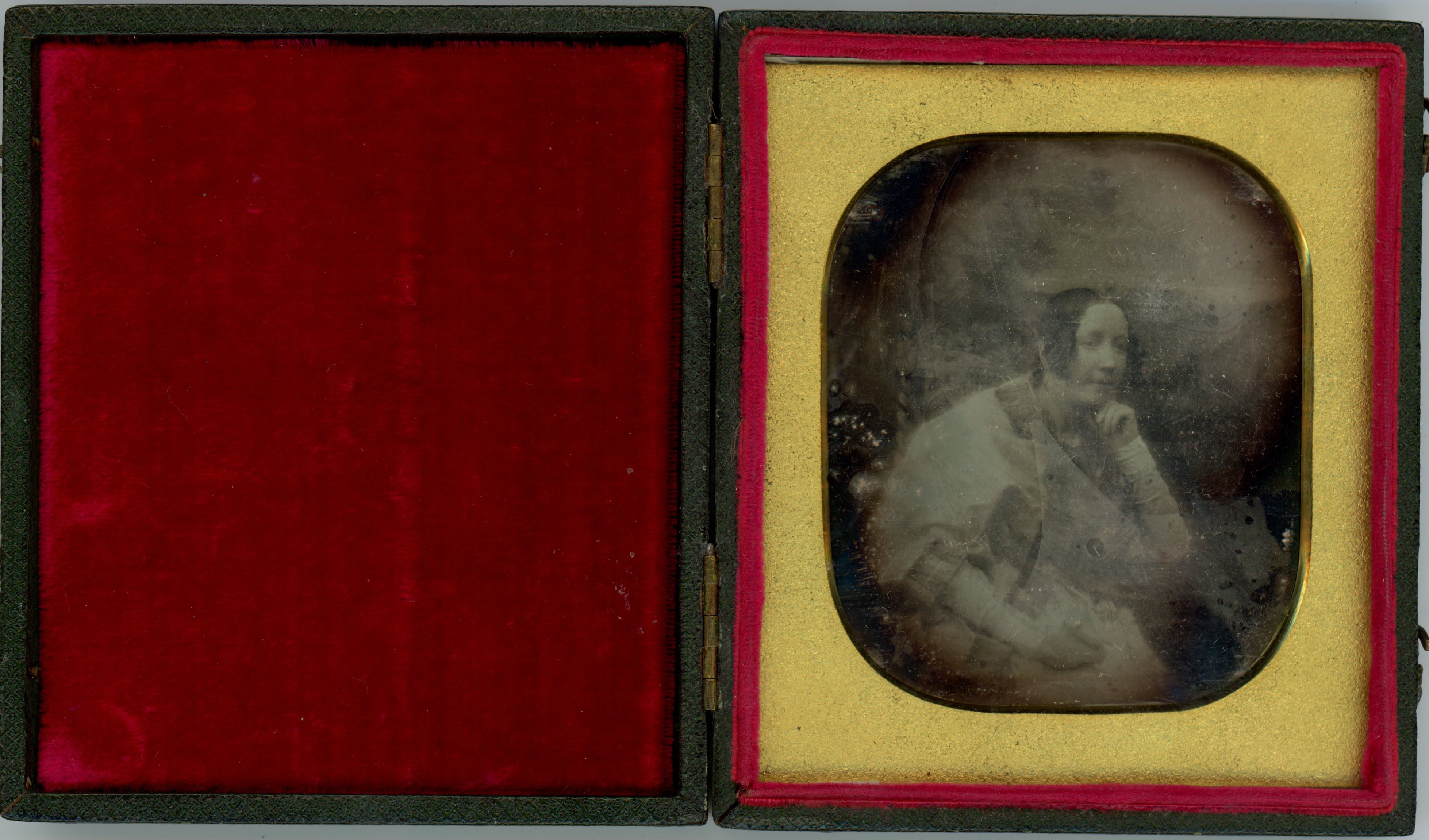 Daguerreotype. A pale-skinned woman with curls framing her long face looks off to our right, chin resting in one hand. The background is difficult to make out due to some abrading or discoloration. The gold mat is rounded at the corner.