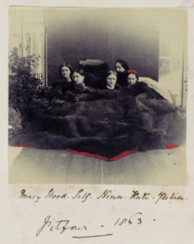 Black and white photograph. Five pale-skinned women sit under a huge dark fur pelt. Red lines have been added along the front edge of the fur, and more red makes a bow on top of one young woman’s head. The women’s names are written in pen below the image, along with “Pitfour 1863”.