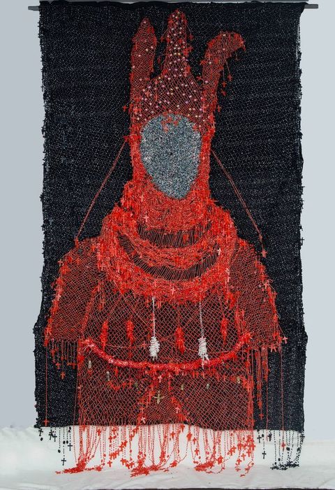 Mixed media. A red silhouette of a costume seems drawn in thread against a black background. The hood has three vertical projections. Tiny red crosses are hung all over the costume, especially around the edges. The space where the face would be is silver.