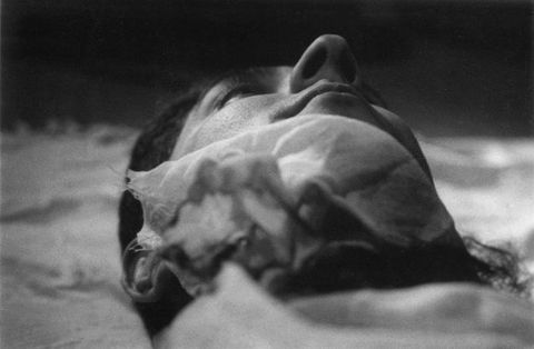 Black and white photograph. The underside of a man’s chin and nose is taken as if the camera was placed on his shoulder or chest. A piece of fabric seems caught up under his chin. His nose is like a peak rising over the mountain range of his face.