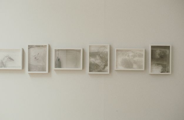 Installation photograph. Six white-framed photographs are printed with silvery, vaporous tones of grey to capture misty, nearly abstract shapes and forms. The photographs alternate between vertical and horizontal orientation.