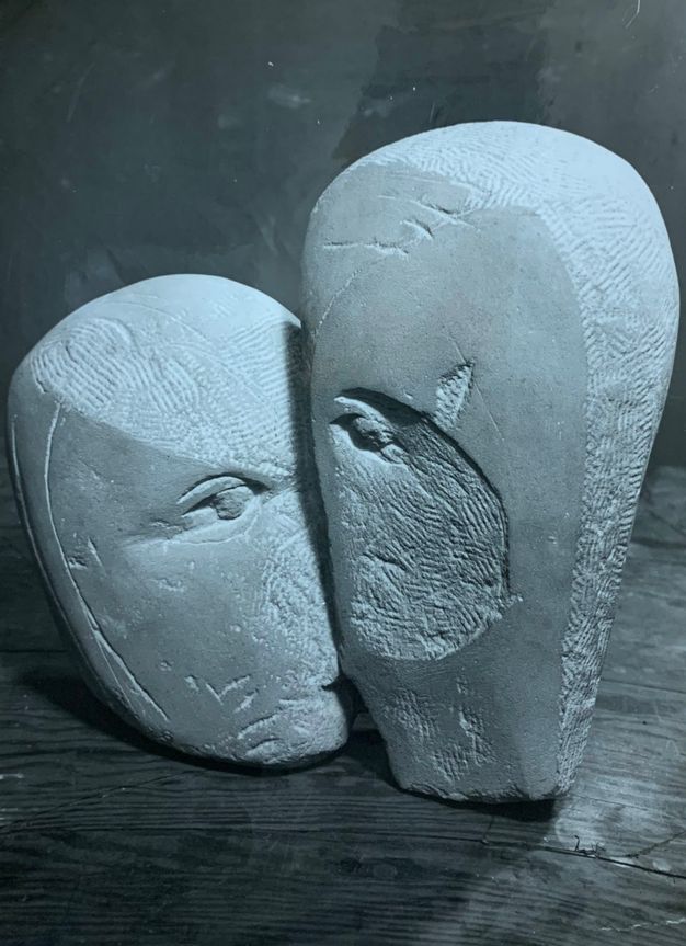 Sculpture. Two roughly oval-shaped stones are carved with one eye each. The eyes are close together, suggesting they may kiss. Some areas of the stone are smooth and others incised with chisel marks.