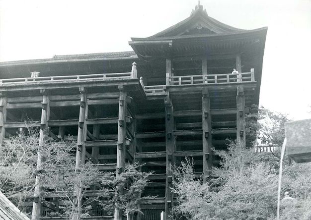 Architecture. We look up at eight storeys of a wooden temple in this black and white photograph. The floors are supported by pillars and the framing is exposed. The roofline is straight to our left, and curves shallowly up to a peak over the three rightmost bays.