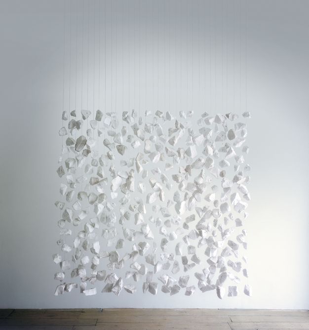 Sculpture. Irregular fragments of white chalk are strung on wires and hung against a white wall so they together form a square.