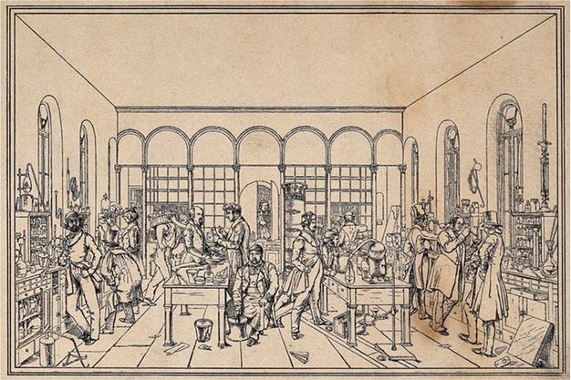 Print. Shown in black lines on light brown paper, men stand or sit at two long tables piled with equipment. Shelves also line the walls, and a few bits of paper and other detritus are scattered on the floor. 