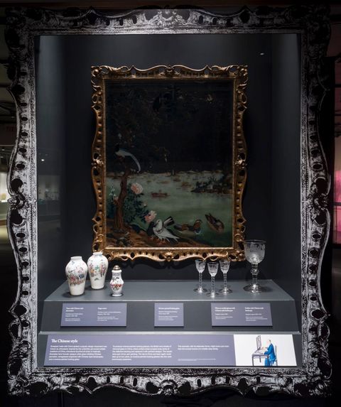 Installation. Porcelain vases, glasses, and a painting in a gold frame are in a case, which is, itself, framed with a duplicate of the gold frame, but in silvery tones.