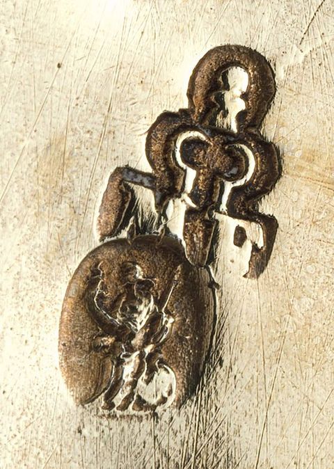 Metalwork. Detail view of a stamp showing a person in an oval under a key-shaped ornament, though the details are difficult to make out.