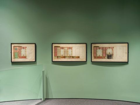 Installation. Three works on paper hang on a mint-green gallery wall. They show designs for red panelling.