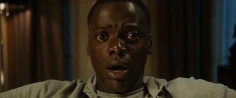 Video still. Close-up view of a dark-skinned man with eyes wide open, tears streaming down his cheeks. His lips are parted.