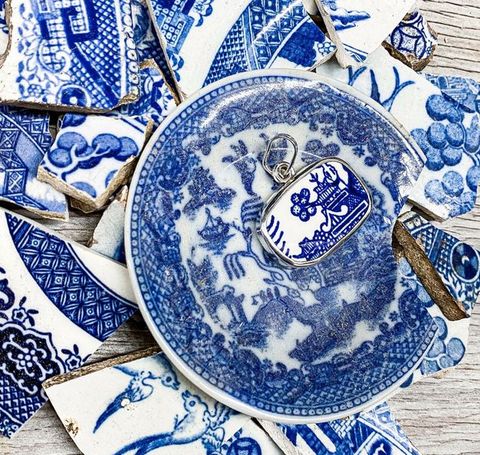 Jewellery. A piece of white porcelain painted in blue with a pagoda is made into a pendant. The pendant sits on a pile of ceramic fragments, all painted with blue against white.