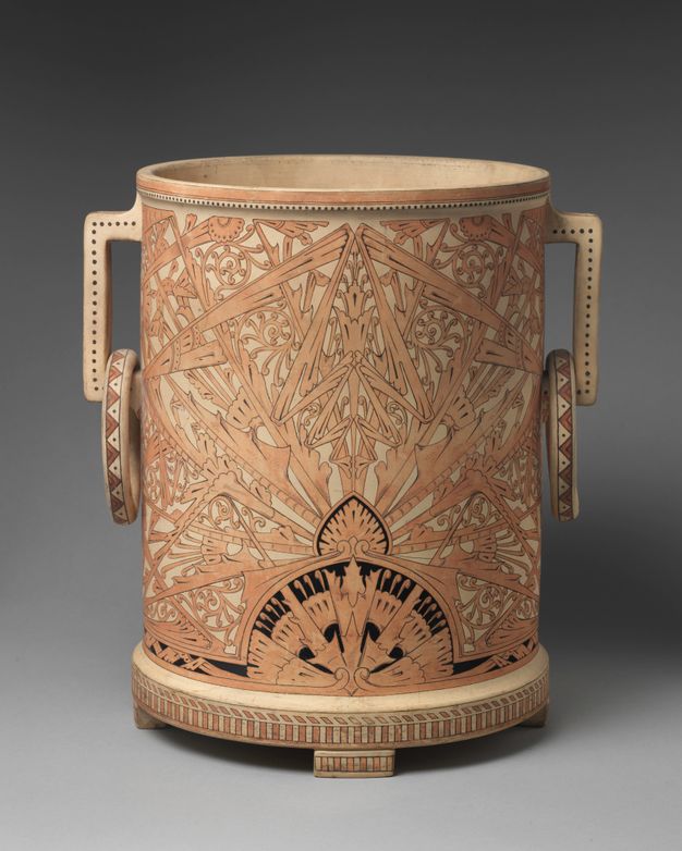 Pottery. Earthenware vessel has a flat, disc-like bottom and straight sides. Rings hang from shallow, straight handles near the lip. The vessel is covered with an intricate pattern of leaves, scrolls, and insect-like bands and forms.
