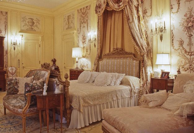 A bed draped with curtains falling from a shallow canopy is set against lemon-yellow panelled walls.