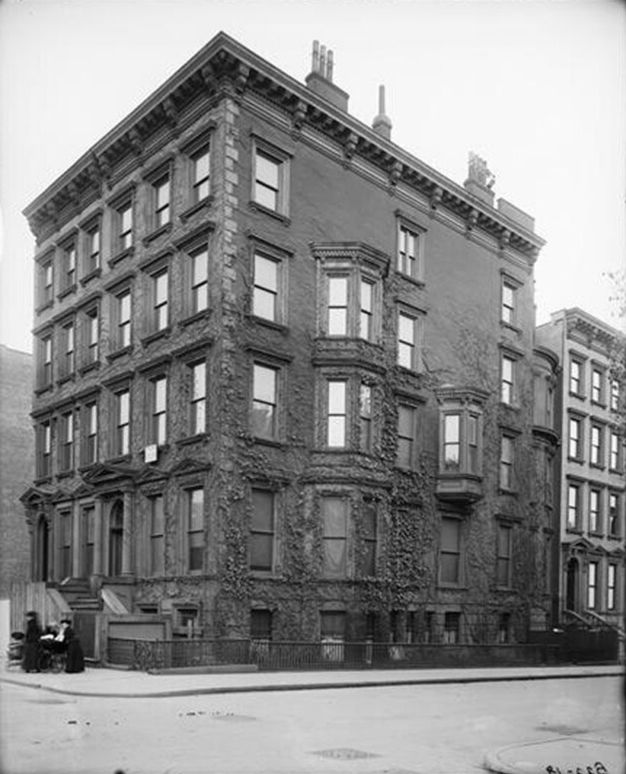 Architecture. A five-storey house is at the corner of a city block. We look at it as if across the intersection from it. The main entrance is on the narrower end, to our left.
