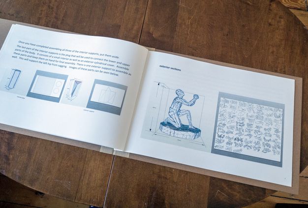 Pages of a book. An illustrated manual instructs the user how to construct a cardboard sculpture showing a kneeling man.