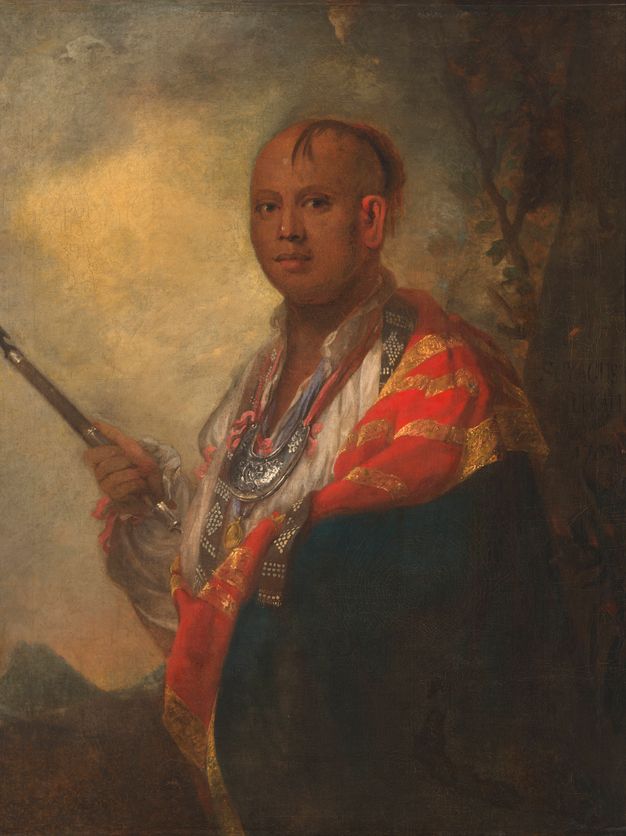 Painting. Shown from the waist up, a medium-skinned man’s body is angled to our left, but he turns to look at us from the corners of his dark eyes. A lock of straight hair falls over his forehead, which is bald over the crown. He wears a white shirt, a crescent-shaped metal gorget low on his chest, and a navy-blue and crimson-red cloak edged with gold.