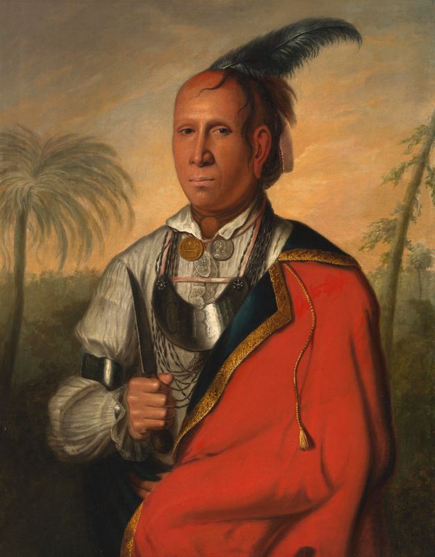 Painting. Shown from the waist up, a medium-skinned man stands in front of a landscape, holding up a knife in one hand. A feather angles back from a mostly bald head. He wears metal medallions, a silver gorget like a thick crescent moon on his chest, and a crimson-red cape or coat over a white shirt.
