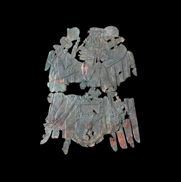 Metalwork. A sheet of metal has been impressed from the back to create a person in low relief. Parts of the sheet are now missing and the copper tarnished. The person faces our left in profile and wears bands around their arms and legs.