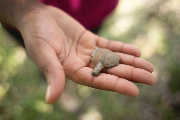 The round end of a silver spoon rests in the hand of a dark-skinned person. The surface of the spoon is pitted and discoloured.