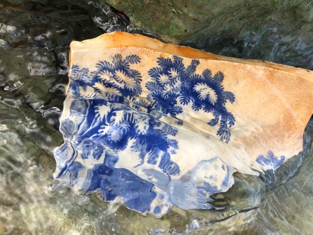 Porcelain. A fragment of white porcelain painted with trees and a mountain in cobalt blue is partially submerged in rippling water.