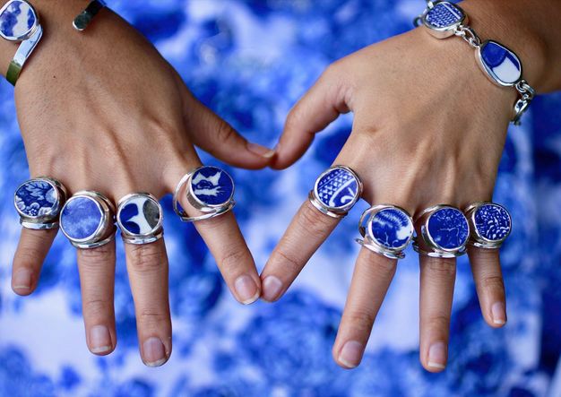 Jewellery. Eight rings and two bracelets are worn on two hands with fingers splayed. Mostly round fragments of white porcelain painted with vivid blue are set in silver.