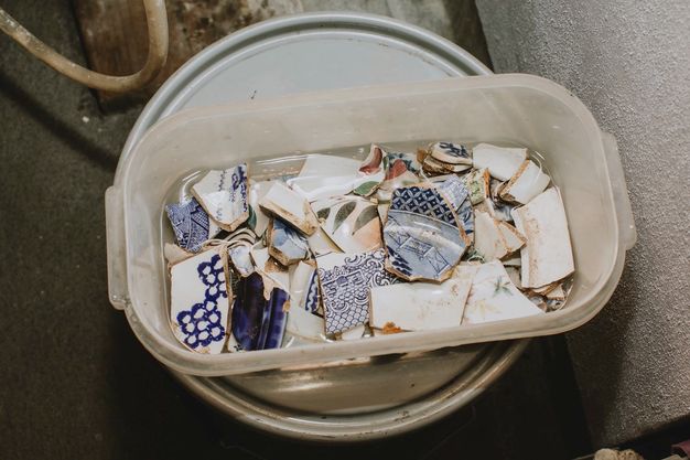 Plastic bin of fragments of white porcelain painted blue, green, or red.