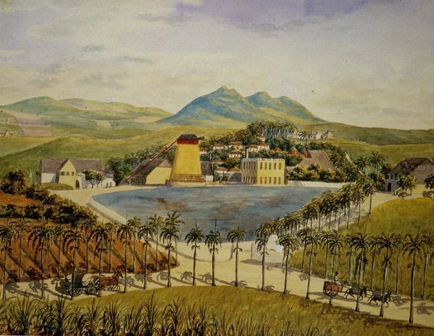 Watercolour. We look down and across at a complex of buildings along and behind the edge of a pond. Palm trees line X-shaped roads that cross the grassy land in front of us and line the pond. Rolling hills move back into the distance.