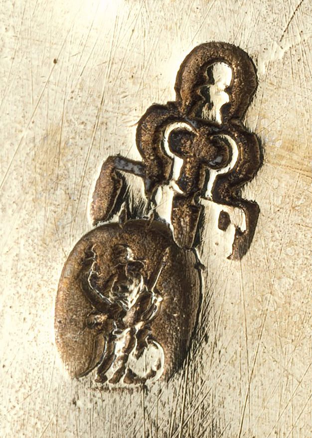 Metalwork. Detail view of a stamp showing a person in an oval under a key-shaped ornament, though the details are difficult to make out.