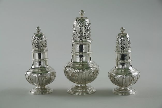 Metalwork. Three different-sized casters would have been used like salt and pepper shakers. Each has an elongated top pierced with x-shaped and lacy designs. They have two-tiered, columnar necks and bulbous bodies over low, flaring feet.