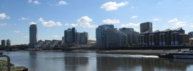Buildings and housing across a rippling river stand against a blue sky.