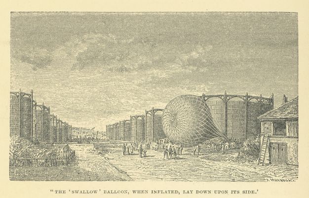 Print. Amid circular storage structures an inflated balloon lies on its side. Dozens of people mill about the fallen balloon.