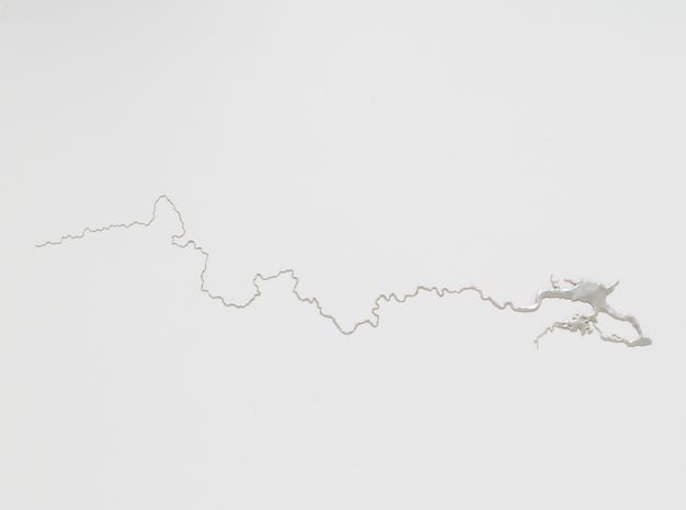 Sculpture. A thread of silver wends towards a thicker rivulet to our right against a white surface.