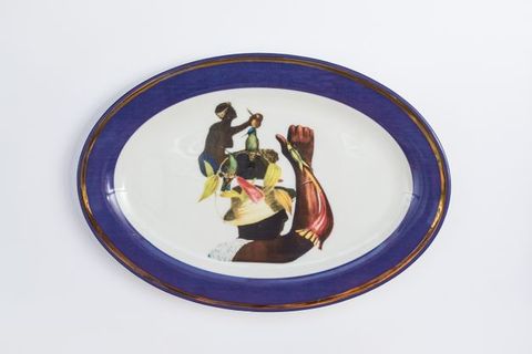 Porcelain. Two dark-skinned women appear collaged with floral elements at the centre of this white oval plate. The cobalt-blue rim is edged in gold.