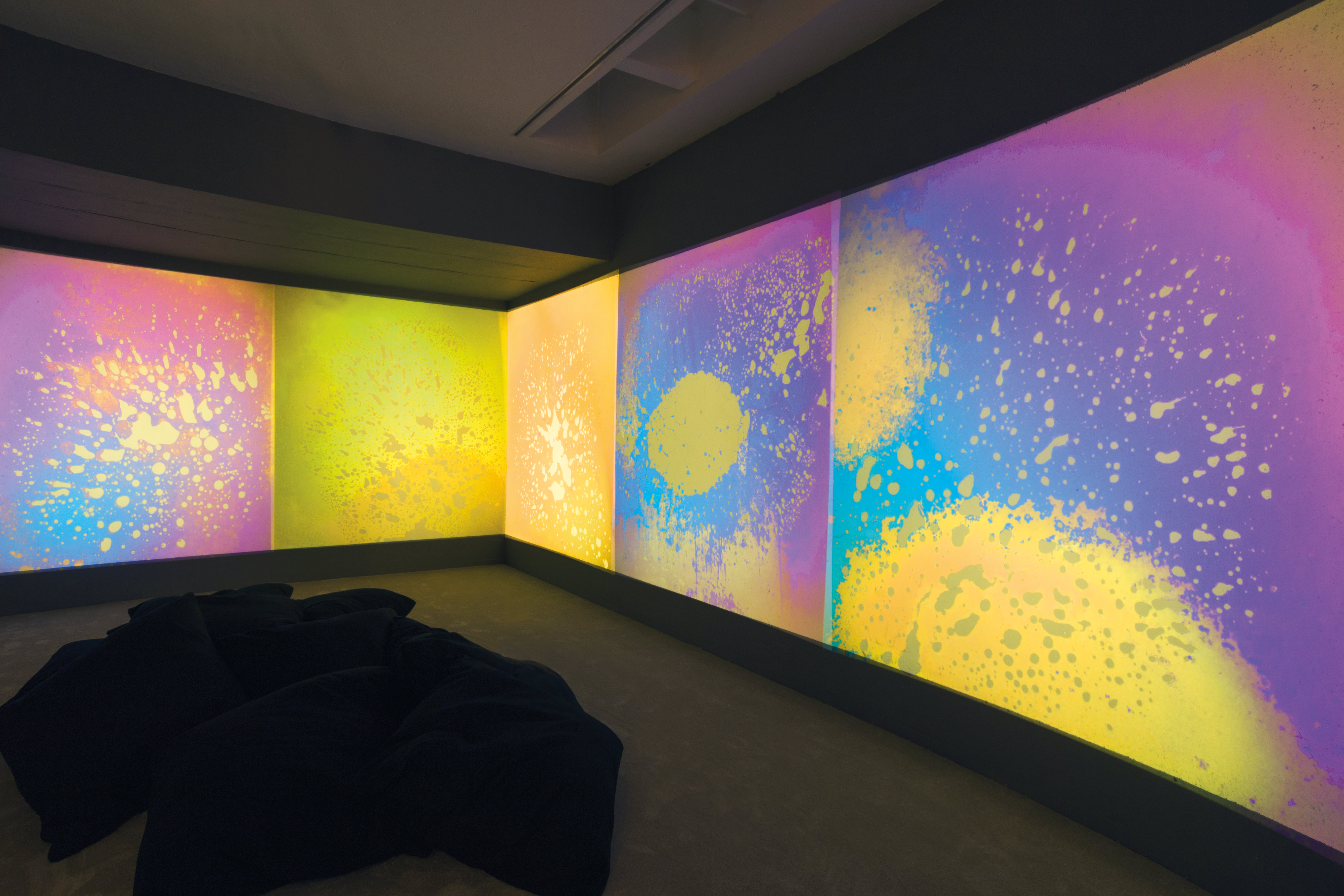 Installation. Clouds and splashes of lemon yellow, rose pink, grape purple, and aqua blue are projected onto gallery walls.
