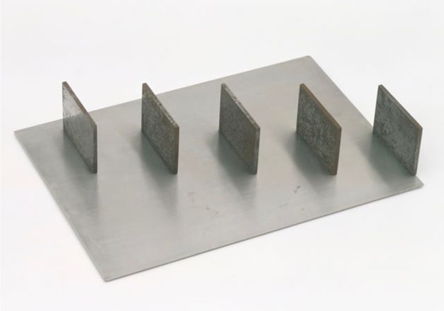 Sculpture. Five metal panels are spaced along a rectangular steel sheet to create a diagonal from one corner to the other. The panels are parallel to each other, like staggered equal signs.