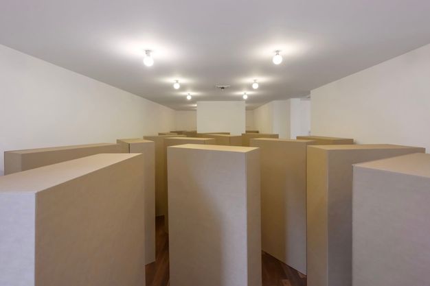 Installation. Rectangular cardboard boxes nearly fill a gallery with white walls and a wood floor.