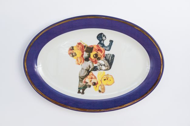Porcelain. Dark-skinned people and other objects in yellow and peach appear collaged at the centre of this white oval plate. The cobalt-blue rim is edged in gold.