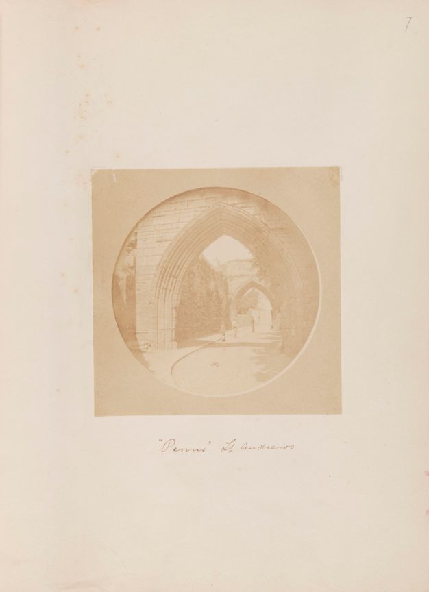 Black and white photograph. In tones of beige and tan, one pointed arch opens onto another, a short distance away down an outdoor path.