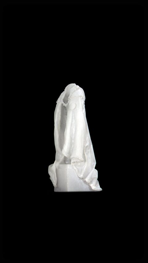 Video still. A white cloak hangs as if over someone’s shoulders, but is empty. The opening is angled to our left against a black background.