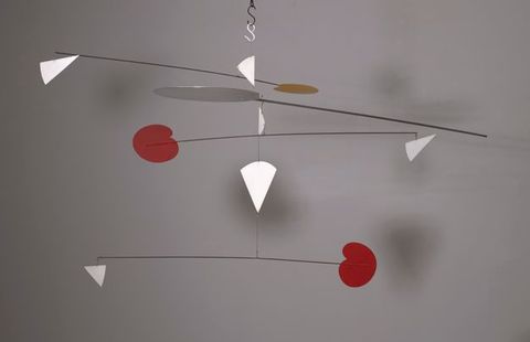 Metal sculpture. Mobile hangs from a ceiling with multi-tiered long thin metal rods extending horizontally out and attaching to red, white, and orange geometric shapes attached to the end of the rods at different angles.