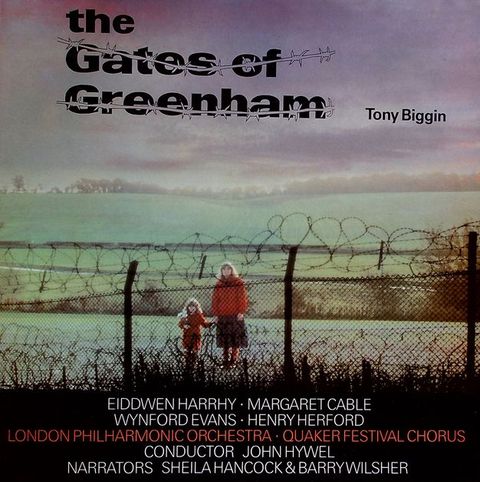 Album cover. A pale-skinned woman and girl hold hands on the far side of a chain-link fence topped with barbed wire. Both have long blond hair, red coats, and they hold hands.