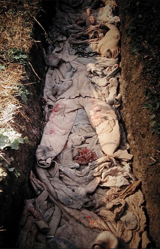 Installation. Stained and bloodied clothing lies in a grave-shaped trench.