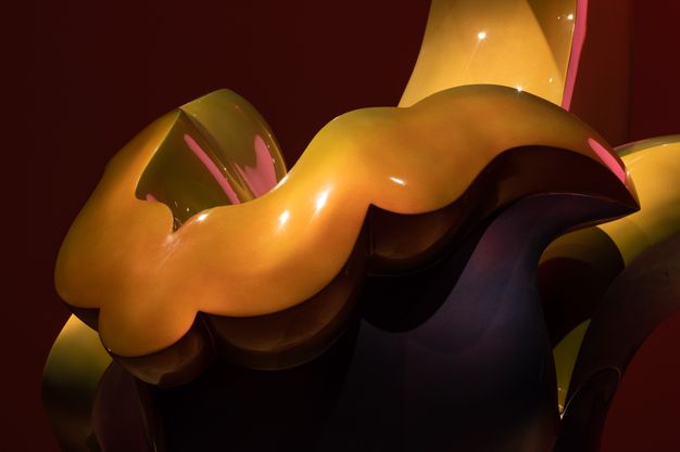 Sculpture. Detail view of the smooth surface of a wavy, honey-gold band.