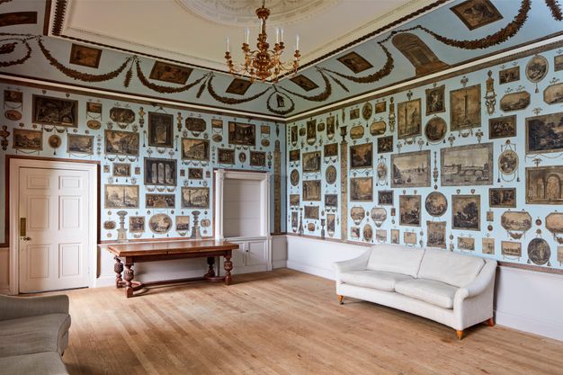 Installation. Dozens of black and white prints in square, rectangular, oval, round, and other formats are pasted to pale blue walls in an elegantly panelled room. More are affixed to the upwards curving cove that connects the wall to the tray ceiling.