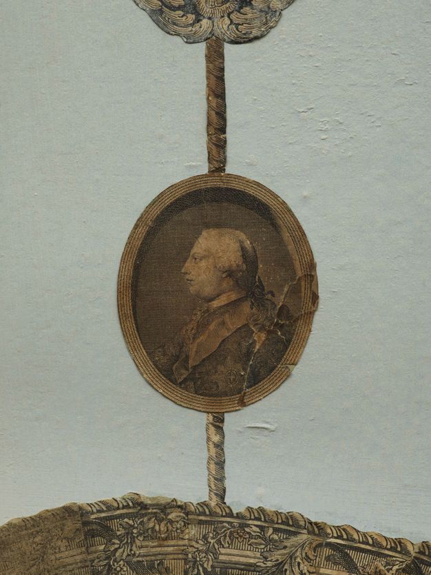 Print. An oval portrait showing a pale-skinned man from the chest up facing our left in profile is affixed to a pale blue wall. Printed ropes above and below connect it to other works, out of view in this detail.