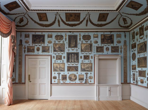 Installation. Prints are affixed to a pale blue wall in an orderly arrangement between and around a door and an alcove.