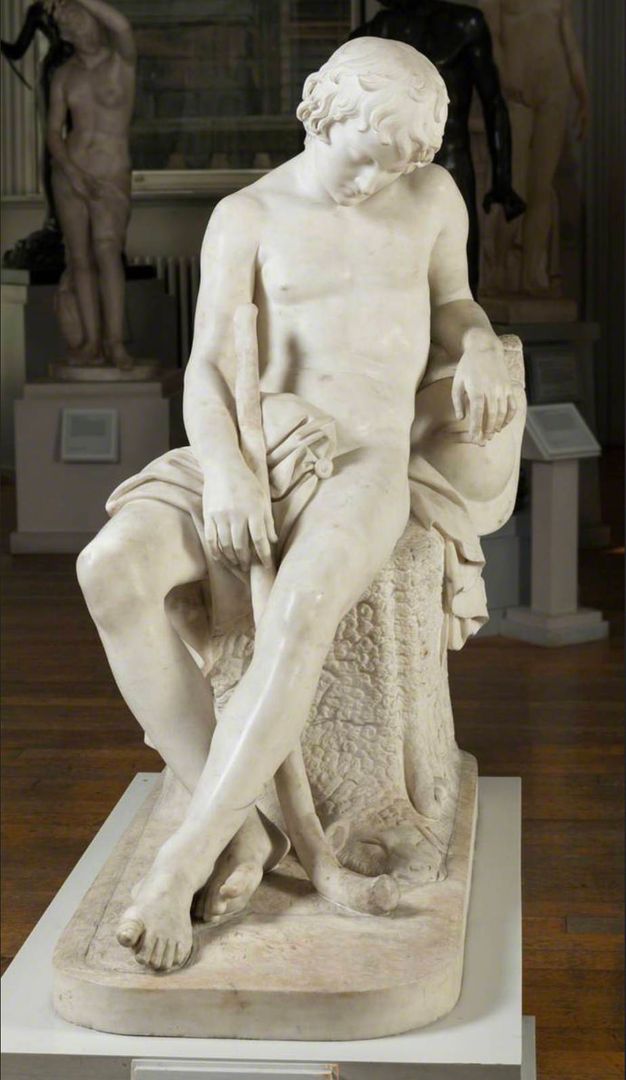 Sculpture. A seated boy’s head falls forwards in sleep in this free-standing sculpture. He leans back onto one elbow. His ankles are crossed, and his other hand rests against a walking stick.