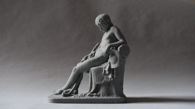 3D printed model. A boy sits and leans back on one elbow, his head falling forwards in sleep. Vertical striations of the printing process are visible in the grey material.