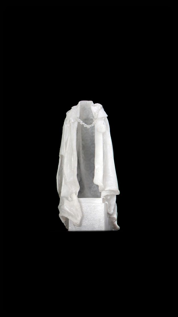 Video still. A white cloak hangs as if over someone’s shoulders, but is empty. A chain connects the lapels across what should be the chest, and the back side is translucent against a black background.