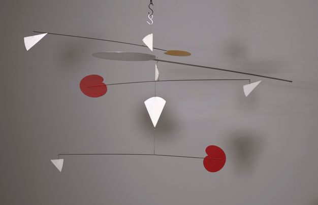 Metal sculpture. Mobile hangs from a ceiling with multi-tiered long thin metal rods extending horizontally out and attaching to red, white, and orange geometric shapes attached to the end of the rods at different angles.